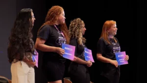 Quatro mulheres em palco de teatro exibindo certificado de premiação do Ela Star 2023